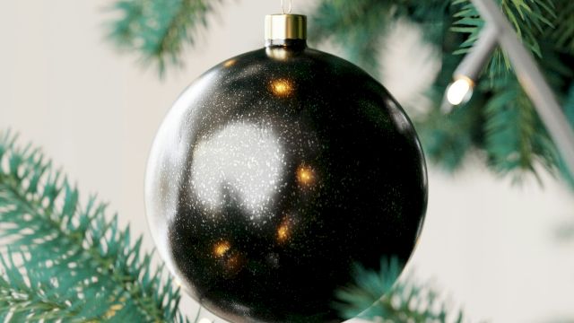 A close-up of a Christmas tree with a shiny black ornament and string lights.